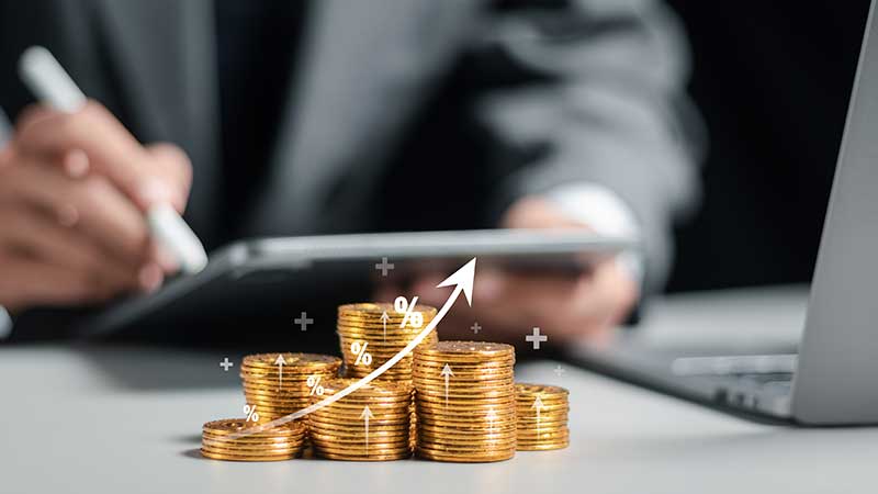 Homem com tablet e montinhos de moedas com o símbolo de percentagem e seta a subir